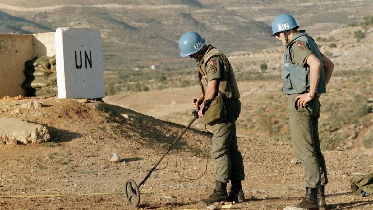 Peacekeepers use metal detection equipment in a vast area.