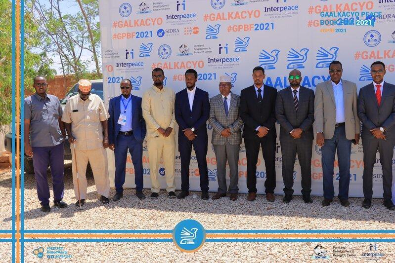 Group of men in front of a backdrop of the Galkacyo Peace Forum 2021